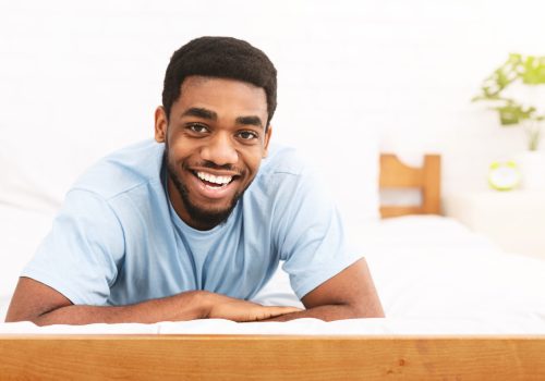 Close up portrait of smiling young african-american man resting in bed at home, panorama with empty space